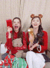 two women are sitting next to each other on a couch holding a teddy bear and a balloon .