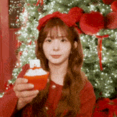 a girl in front of a christmas tree holding a cupcake with a snowman on top