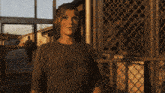 a woman standing in front of a chain link fence with a man walking behind her