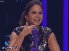 a woman in a sequined top is smiling and holding a purple microphone with the hashtag lialmeida05
