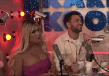 a man and a woman are sitting in front of microphones in front of a sign that says thank you .