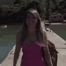 a woman in a pink dress is smiling while walking on a dock .