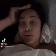 a woman is laying in bed with her hand on her forehead and a tiktok watermark on the bottom right