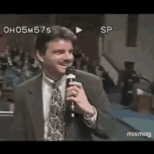 a man in a suit and tie is holding a microphone and smiling in front of a crowd .