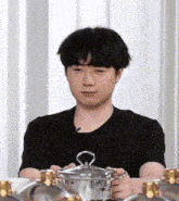 a man in a black shirt is holding a pot with a lid .