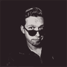 a black and white photo of a man wearing sunglasses and a black shirt .