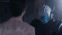 a man in a pink shirt is looking at a robot with a blue mask