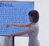 a woman stands in front of a screen with korean writing