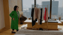 a woman in a green coat stands in a bedroom