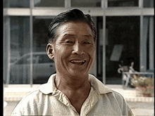 a man in a white shirt is smiling in front of a glass building