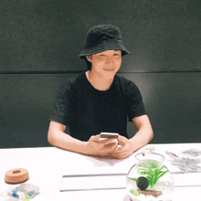 a person wearing a black hat is sitting at a table looking at a cell phone