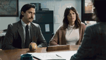 a man and woman are sitting at a desk with an apple on the desk