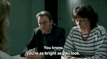 a man and woman are sitting at a table and the woman says you know you 're as bright as you look