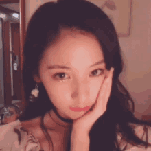 a woman with her hand on her face is wearing a choker and earrings