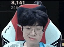 a young man wearing glasses is sitting in a chair with a cat ear pillow .