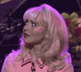 a woman with blonde hair and pink makeup is standing in front of a piano and flowers .