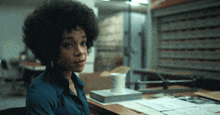 a woman in a blue shirt sits at a desk with a white mug on top of a book