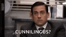 a man in a suit and tie is sitting at a desk and saying `` cunnilinguas '' .