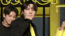 a man in a black jacket and yellow tie is making a funny face while another man looks on .