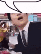 a man in a suit and tie is talking with a speech bubble above him .