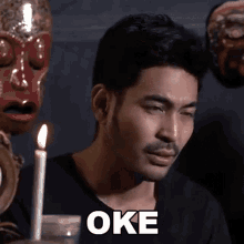 a man sitting in front of a candle with the word oke on his face .