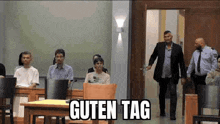 a group of people are sitting in a courtroom with the words guten tag written on the screen .