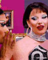 a woman whispering into another woman 's ear while wearing a necklace and earrings