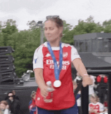 a woman wearing a red emirates fly better shirt is holding a bottle of water
