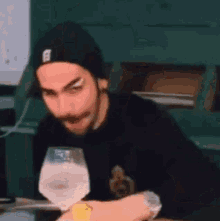 a man with a beard is sitting at a table with a glass of wine .