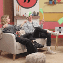 a man and a woman sitting on a couch with a sign that says smosh on it