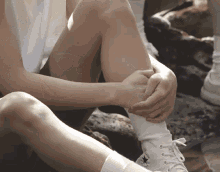 a person wearing a pair of white converse shoes sits on a rock