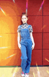 a girl wearing overalls and a plaid shirt is standing in front of an orange wall .