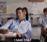 a man is sitting at a desk in a classroom and saying " i said that "