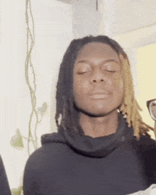 a young man with dreadlocks is wearing a black hoodie and glasses .