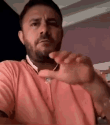 a man with a beard is wearing a pink shirt and making a funny face with his hand .