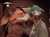 a man in a green hat smoking a cigarette next to a puppet