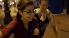 a woman wearing glasses and a red shirt is smiling while standing next to another woman .