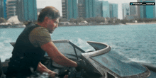a man is driving a boat in the water with a city in the background and a watermark that says pranay varma