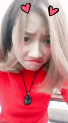 a girl wearing a red shirt and a black necklace has two hearts drawn on her hair