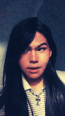 a close up of a person 's face with long hair and a cross necklace