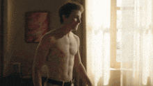 a shirtless man stands in front of a window in a room