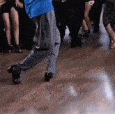 a man in a blue shirt and grey pants is dancing on a wooden floor
