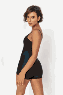 a woman in a black dress is standing in front of a white wall