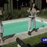 a woman in a crop top is dancing in front of a swimming pool with a sign that says las