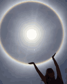 a woman is holding up her hands in front of a circle of light .