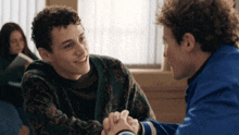 two young men are holding hands in a classroom and smiling