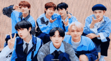 a group of young men in blue shirts are posing for a picture and making peace signs .