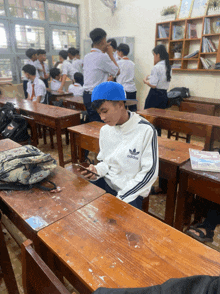 a boy wearing a white adidas jacket sits at a desk