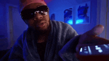 a man wearing sunglasses and a pink hat is holding a cell phone in his hand .