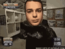 a man is standing in front of a shelf with the time 6:08 on the screen behind him .